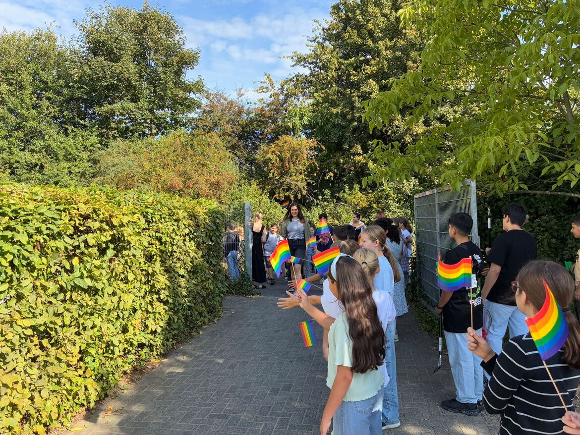 Kinder stehen mit bunten Regenbogenfähnchen am Eingang